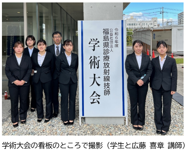 学術大会の看板の前で、スーツを着た学生たちが集合している様子。