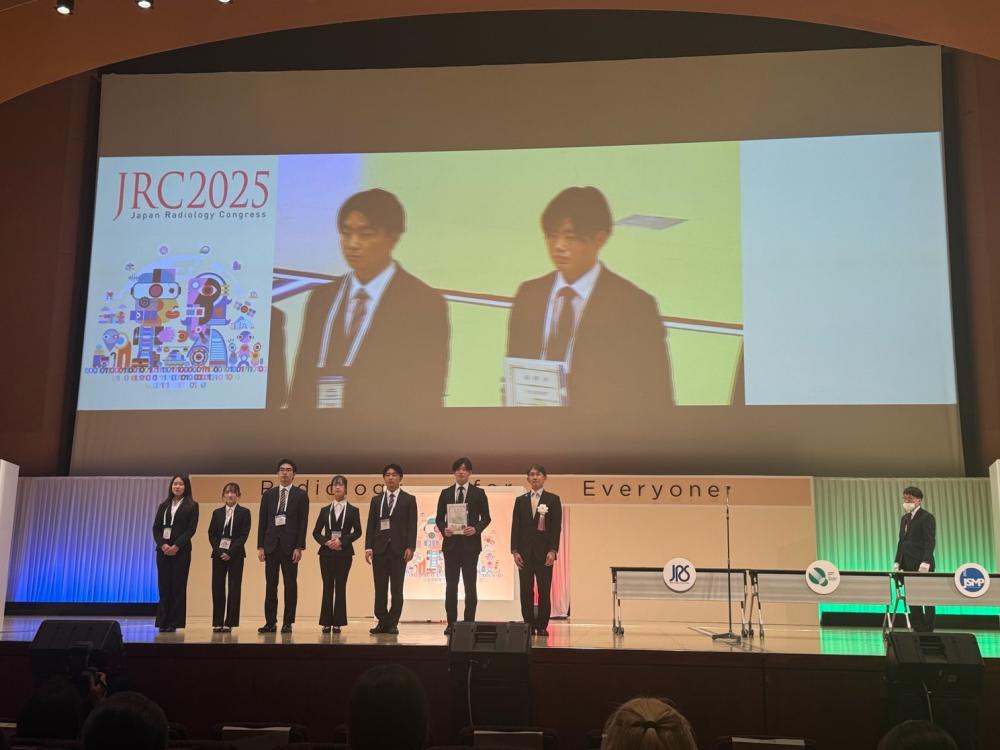大学院生が放射線医学会で受賞し、壇上で表彰される様子。背景には「JRC2025」のロゴが見える。