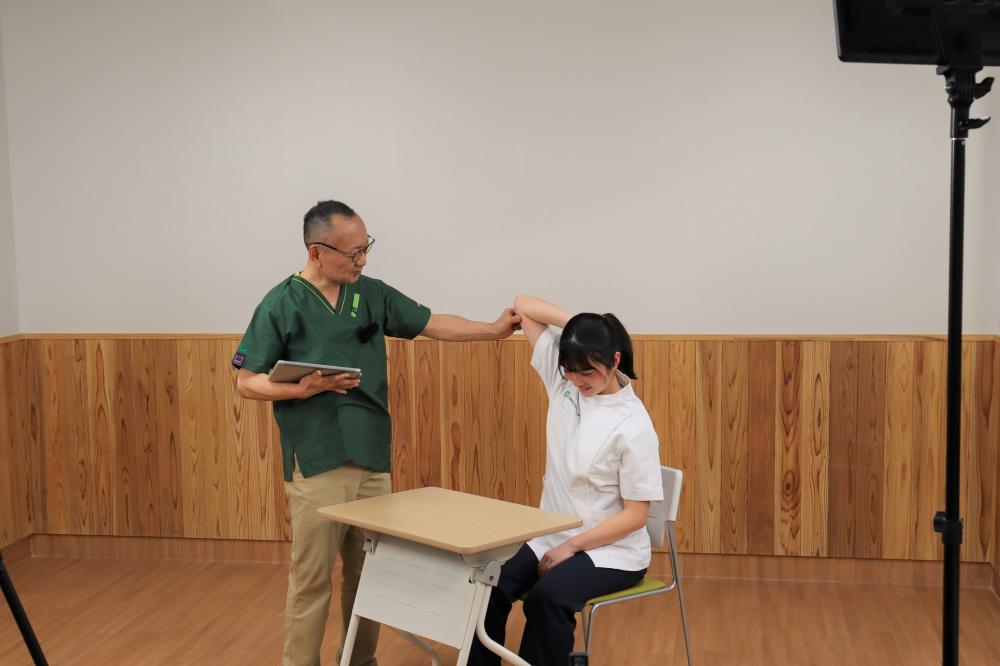 医療現場での指導風景。医師が患者の腕をチェックしている様子。