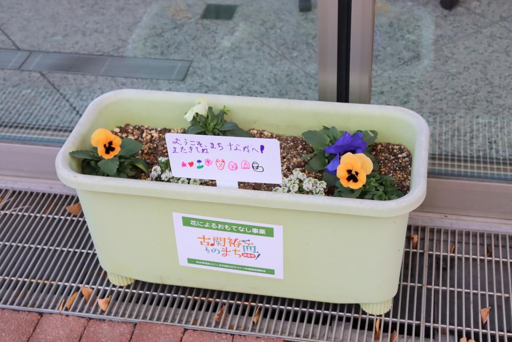 プランターに植えられた花々と手書きのメッセージが添えられた風景。