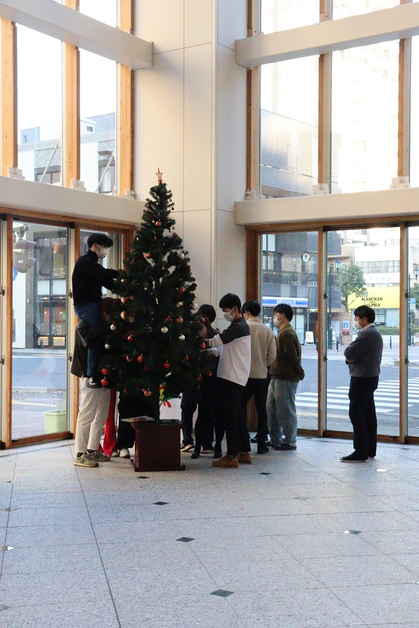 クリスマスツリーの飾り付けを行う人々が集まる室内の様子。