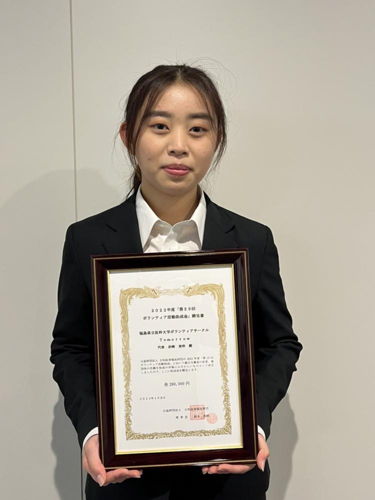 ボランティアサークルのメンバーが福祉財団助成金の証書を持って微笑んでいる写真。