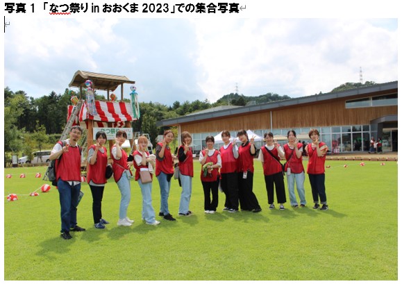 ボランティアサークルのメンバーが「なつ祭り」で笑顔でポーズをとる様子。背景には緑の芝生と建物が見える。