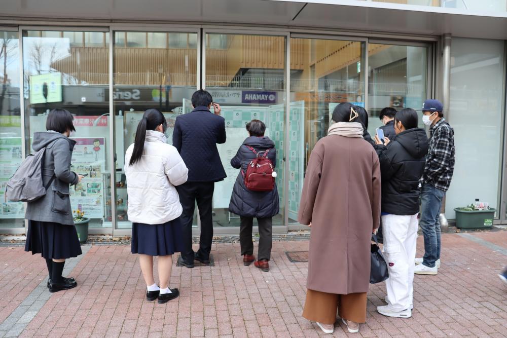 合格発表を待つ学生たちが、福島駅前キャンパスのエントランスホール前で掲示板を見つめている様子。