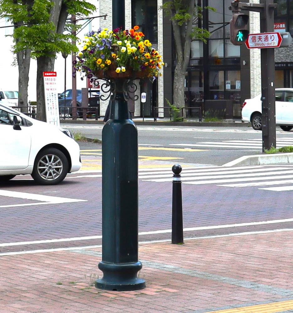 街路灯に色とりどりの花が飾られたフラワーバスケットが設置されている風景。