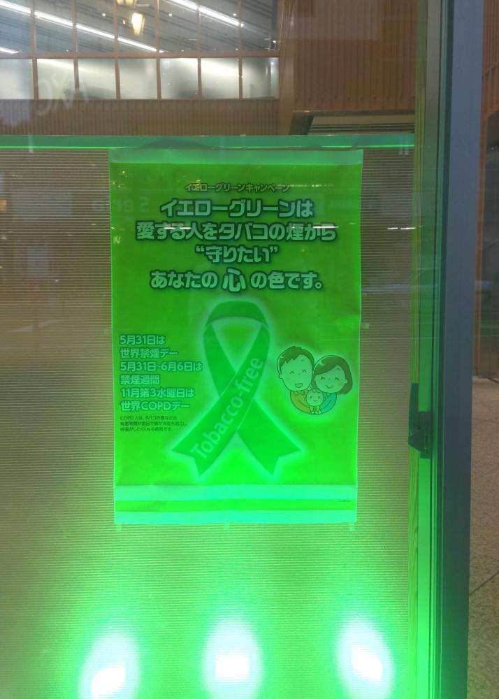 イエローグリーンキャンペーンのポスターが、緑色のライトに照らされている様子。受動喫煙防止の啓発を目的とした内容が記載されています。