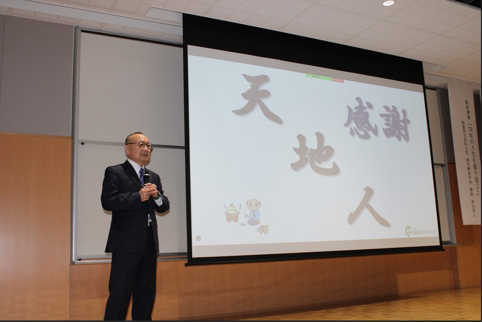 神先秀人教授が最終講義で「感謝」をテーマに話している様子。背景には「天」「地」「人」の文字が表示されています。
