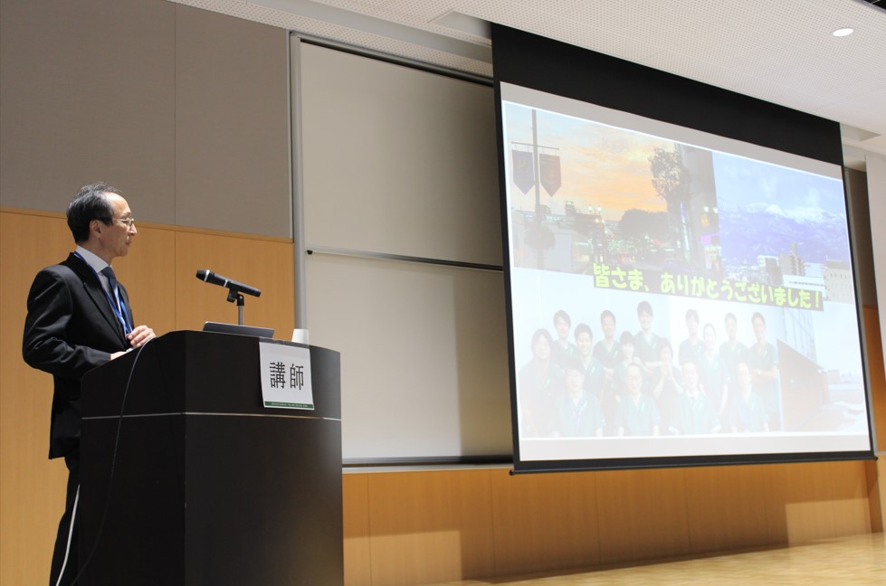 神先秀人教授が講義を行い、スライドには風景や研究チームの写真が映し出されています。