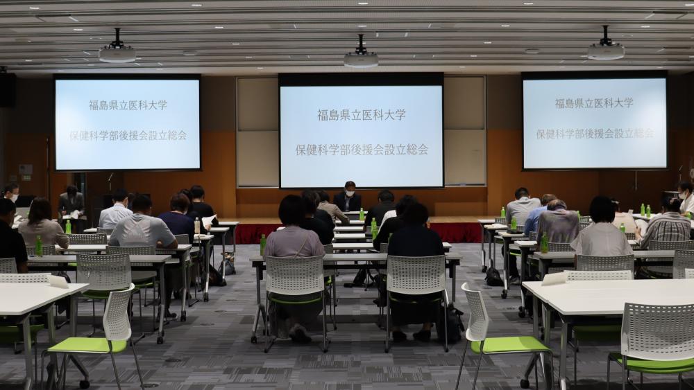 福島県立医科大学の講義室で行われている会議の様子。参加者が座っており、スクリーンには大学名が表示されている。