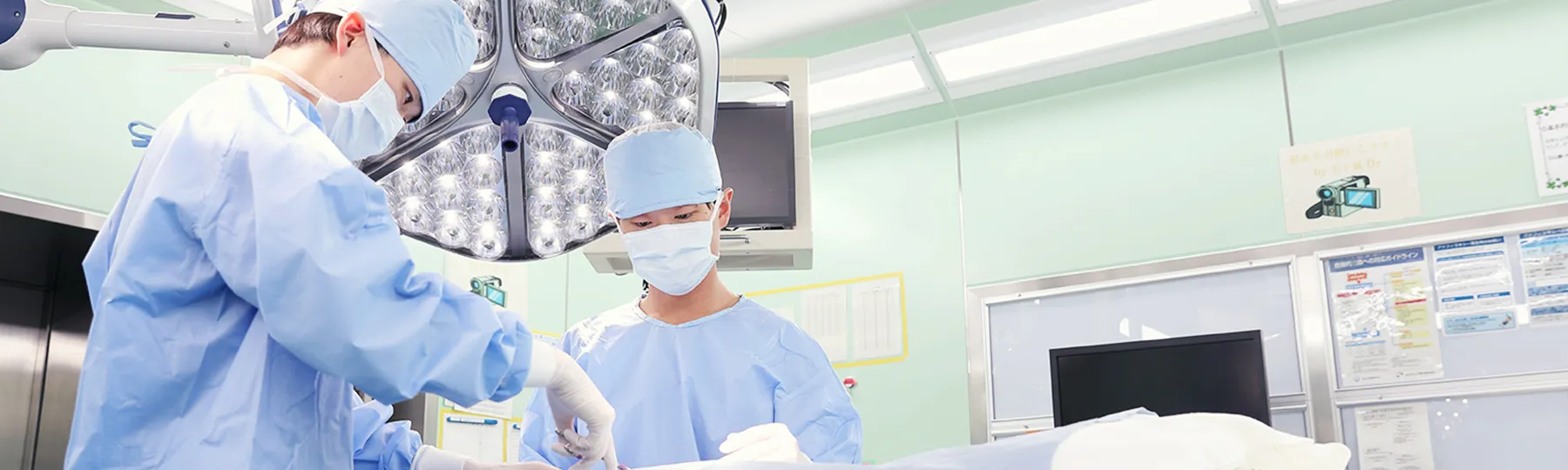 手術室で医療従事者が手術を行っている様子。青い手術着を着た二人の医師が患者に集中している。