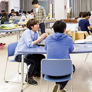 学生たちがテーブルを囲んで話し合い、学び合う様子が見られる教室の風景。