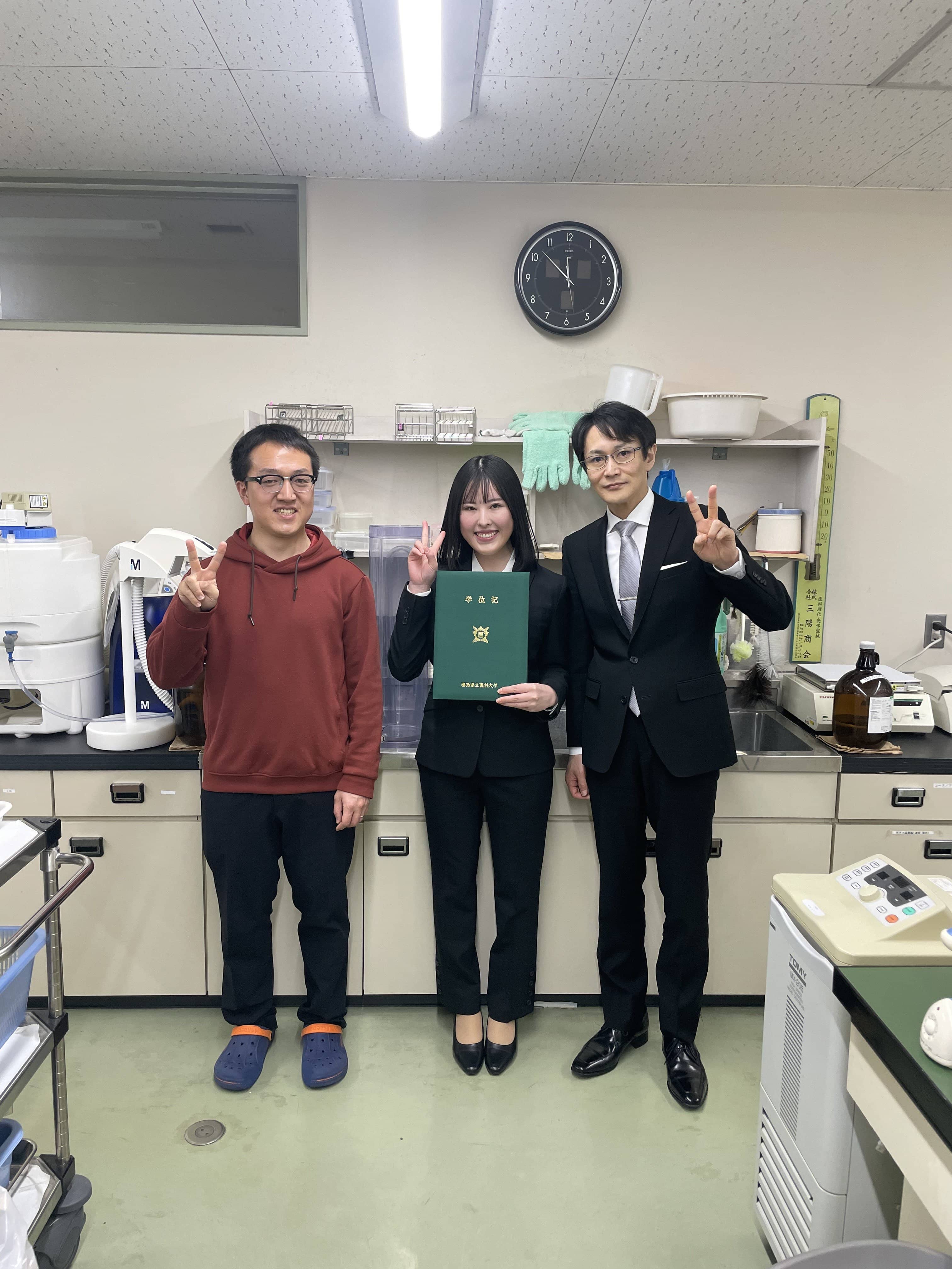 MD-PhDプログラムの卒業生たちが、研究室で卒業証書を持って笑顔でポーズをとっている写真。
