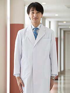 福島県立医科大学の乳腺外科学講座の学内講師、白衣を着た男性が廊下で微笑んでいる様子。