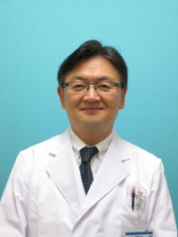 教授の石田隆史が白衣を着て微笑んでいるポートレート。背景は青色。