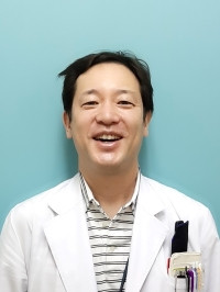 准教授の小林淳が白衣を着て微笑んでいるポートレート。背景は淡い青色。