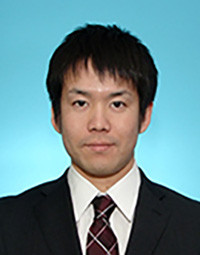 助教の佐藤悠さんのプロフィール写真。青い背景の前でスーツを着て微笑んでいる。