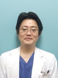 准教授の山田慎哉氏が白衣を着て微笑んでいるポートレート。背景は淡い青色。