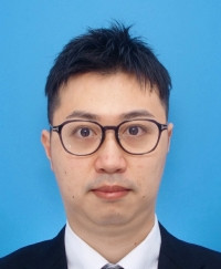 専攻医の堀岡暉が青い背景の前で正面を向いている写真。