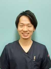 医療用の服を着た男性が微笑んでいるポートレート。背景は淡い青色。