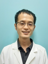 医療用白衣を着た男性が微笑んでいるポートレート。背景は淡い青色。