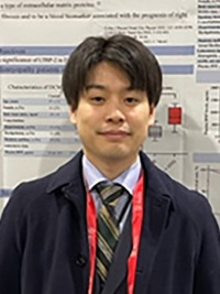 大学院生の西浦司人が研究発表のポスターの前で微笑んでいる写真。