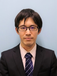 大学院生の大和田光司さんがスーツを着て微笑んでいるポートレート。背景は淡い青色。