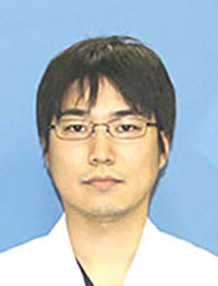 大学院生の坂本和哉さんのポートレート。白衣を着て、眼鏡をかけた真剣な表情。背景は青色。