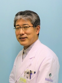 福島県立医科大学の教授、中里和彦氏が白衣を着て微笑んでいるポートレート。背景は淡い青色。