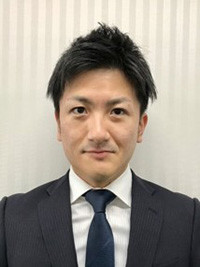 大学院生の大橋尚人さんがスーツを着て微笑んでいるポートレート。背景はシンプルなストライプ模様。