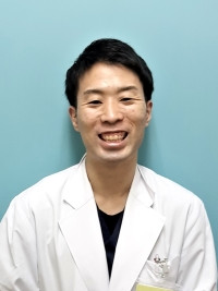 大学院生の佐藤勇太朗が白衣を着て微笑んでいるポートレート。背景は淡い青色。