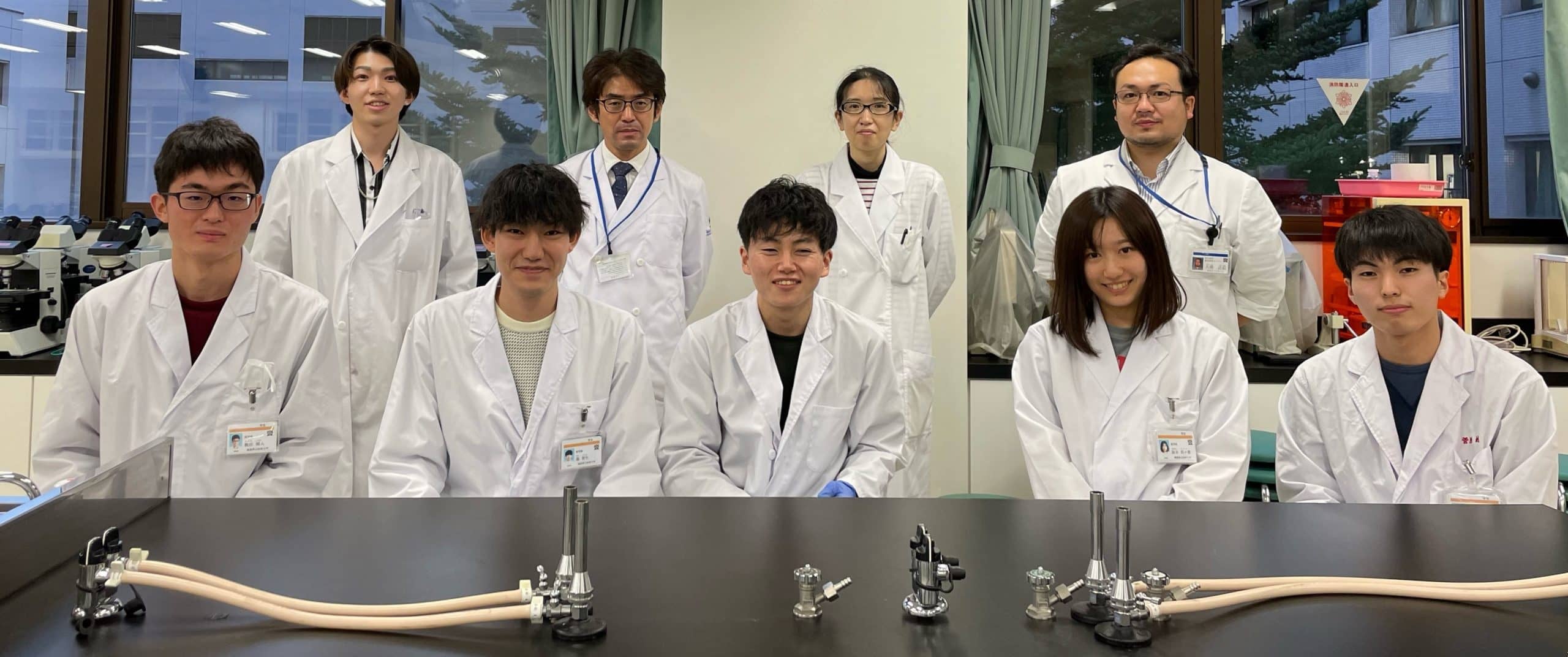 医学部1年生の有志が化学実験を行っている様子。白衣を着た学生たちが実験器具の前に集まっている。