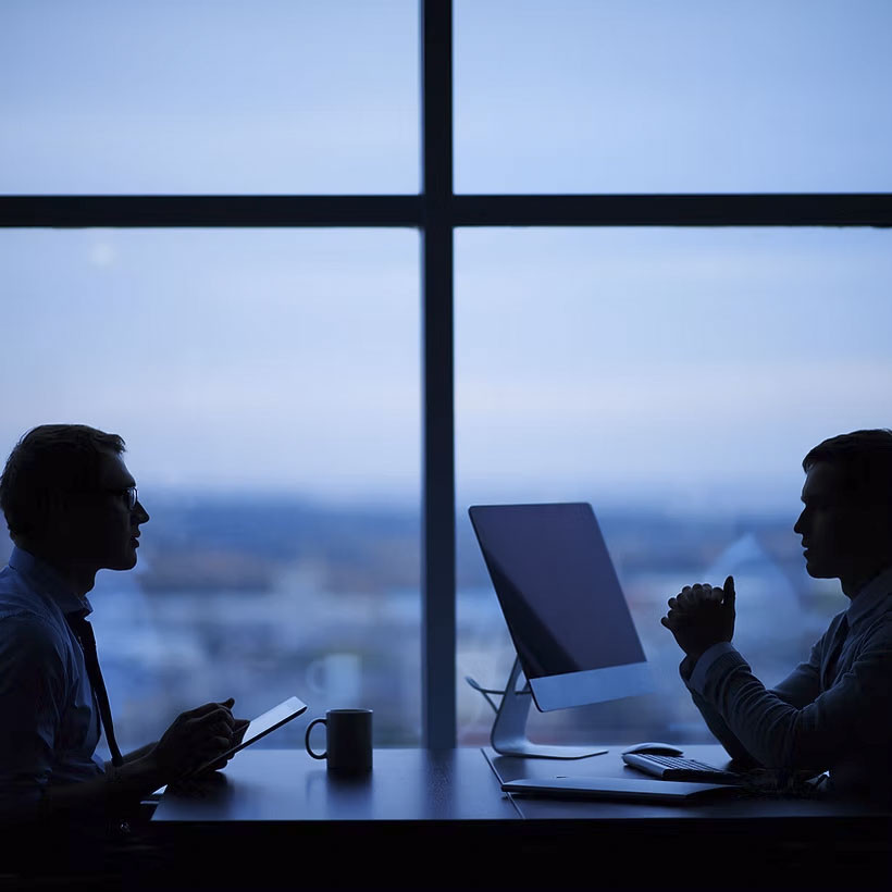 二人の人物が机を挟んで対面し、ビジネス会議を行っているシルエット