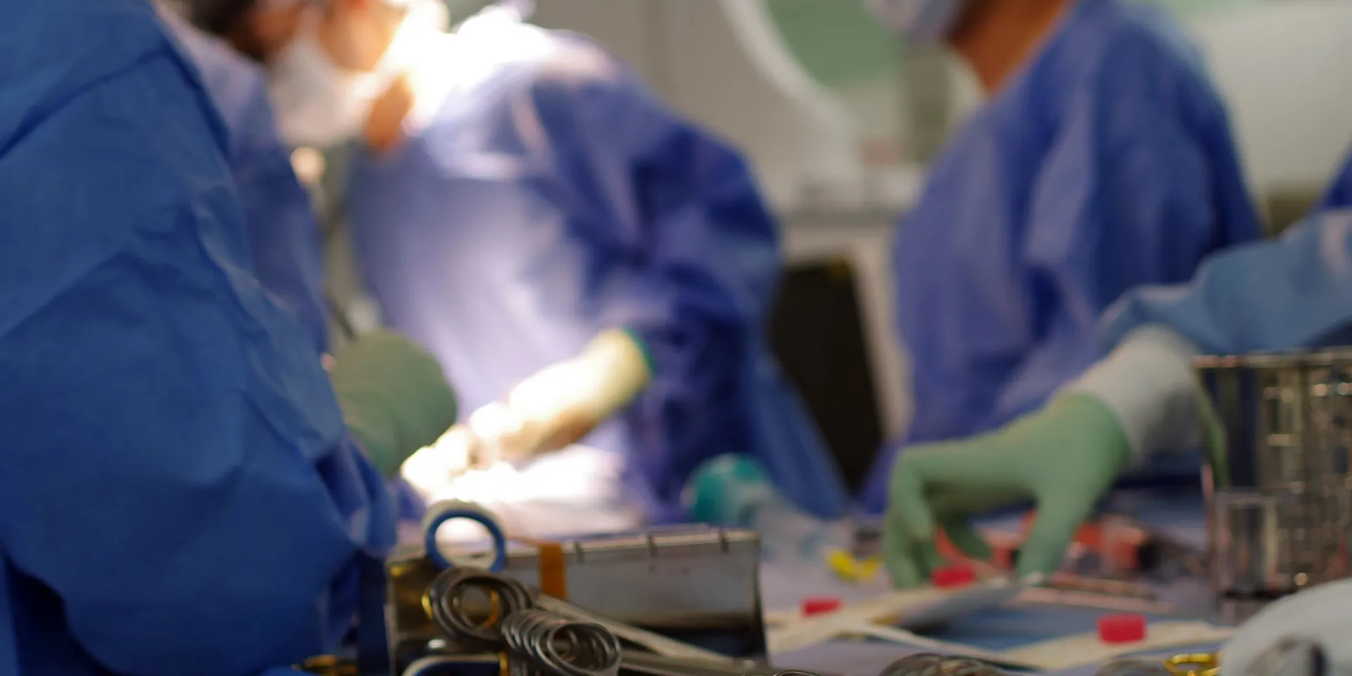 手術室で医療スタッフが心臓手術を行っている様子。青い手術着を着た医師たちが器具を扱っている。