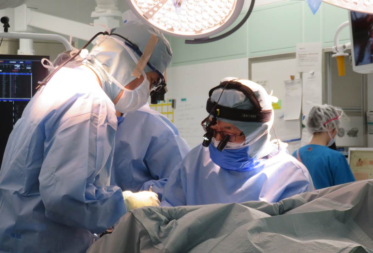手術中の医師が特別な拡大鏡を装着し、集中している様子。背景には他の医療スタッフが見える。