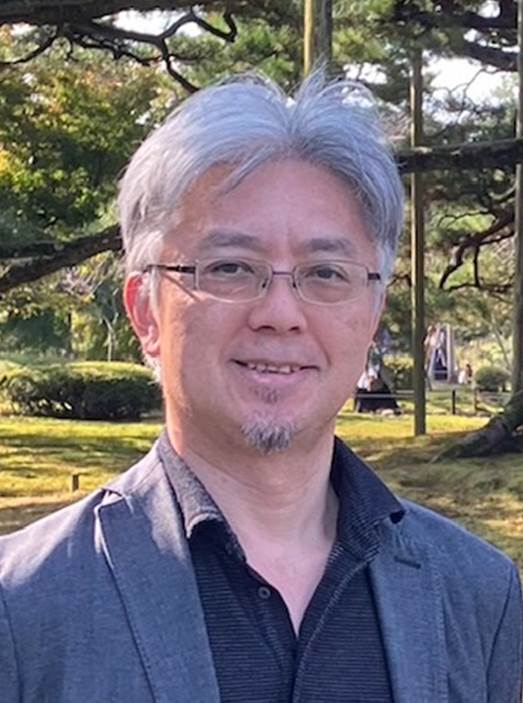 准教授の若松大樹医学博士が公園で微笑んでいる写真。背景には緑豊かな木々が見える。