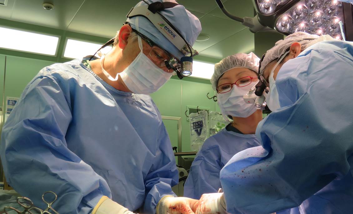 手術室で医療スタッフが心臓手術を行っている様子。青い手術着を着た医師たちが器具を扱っている。