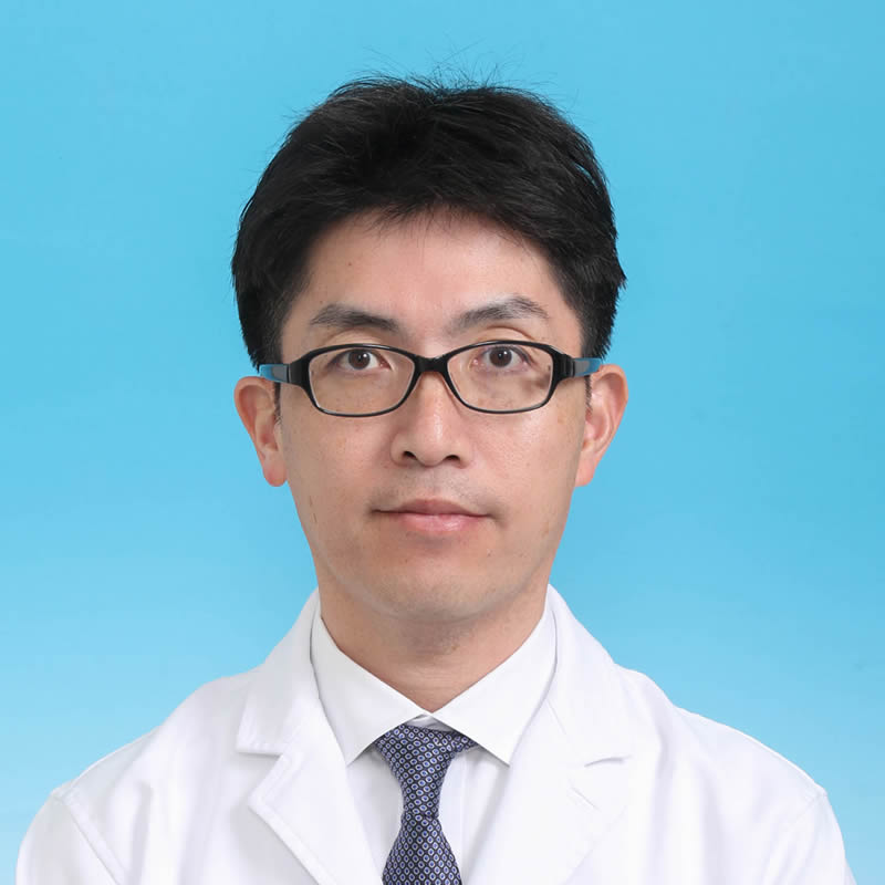 主任教授の古屋文彦氏が白衣を着て、青い背景の前で微笑んでいるポートレート。