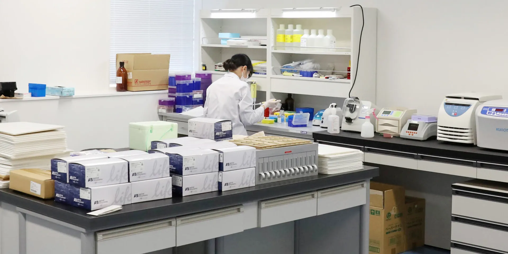 研究室で実験を行う研究者が、試薬や器具を使っている様子。机の上には多くの実験用具や試薬が整然と並んでいる。