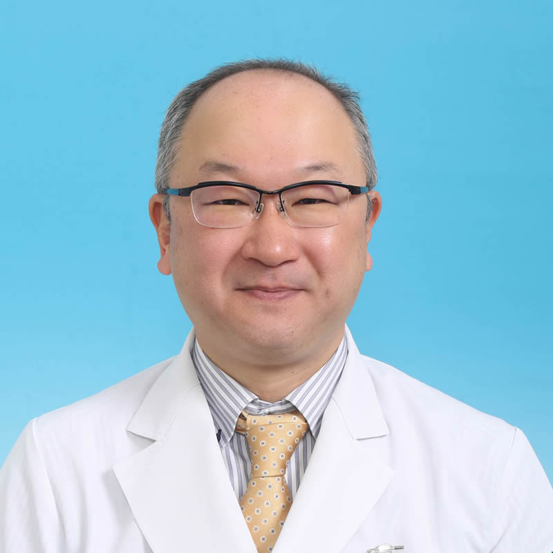 医療白衣を着た鈴木聡講師のポートレート、明るい青い背景。