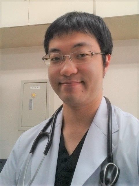 医療用白衣を着た田辺隼人医師が微笑んでいる自撮り写真。
