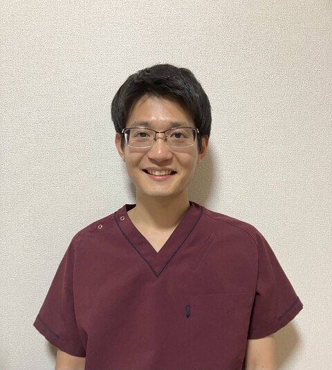 スタッフの取出俊平さんが医療用の服を着て微笑んでいる写真。