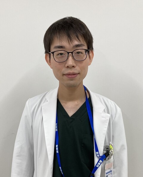 医療白衣を着た矢吹峻也さんが、カメラに向かって微笑んでいるポートレート。