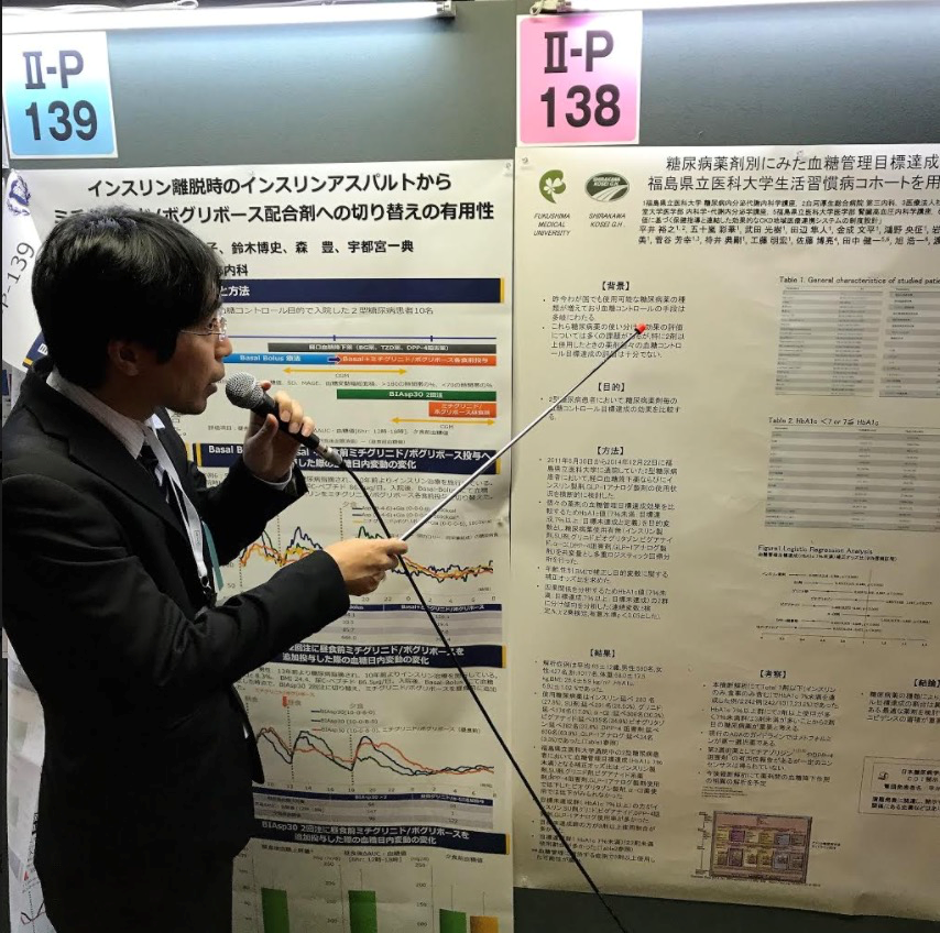 博士研究員の平井裕之がポスター発表を行っている様子。研究内容を説明しながら指示棒を使って資料を指し示している。
