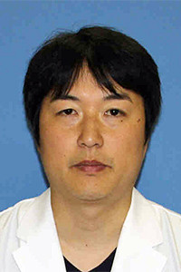 医療白衣を着た渡辺洋平医師のポートレート。背景は青色。