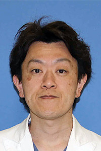 医師の小野澤寿志氏の顔写真。白衣を着用し、青い背景の前で微笑んでいる。