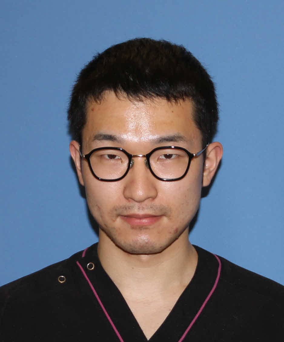 長谷川誠医師のポートレート、黒い医療用ユニフォームを着用し、青い背景の前で微笑んでいる。