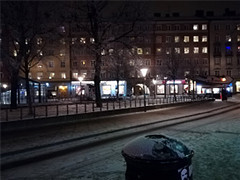 スウェーデンの夜の街並み、雪が積もった通りと明かりが灯る商業施設が見える風景。