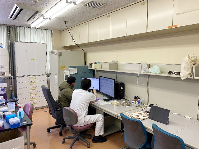 カンファレンス室でコンピュータを使っている二人の研究者の様子。机の上には実験器具や資料が散らばっている。