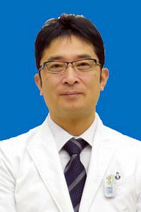 特任教授の大木進司氏が白衣を着て微笑んでいるポートレート。背景は青色。