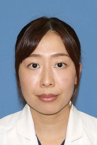 伊藤美郷助教のプロフィール写真。白衣を着た女性が青い背景の前で微笑んでいる。